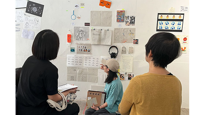 林芸慈坐在她經常使用的榻榻米坐墊上，與現場同學們分享她的創作。（周幸瑤拍攝）